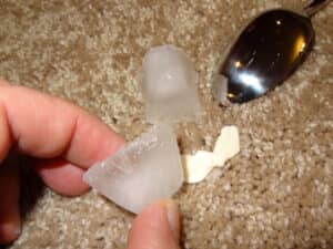 Person using ice and a spoon to remove gum from carpet